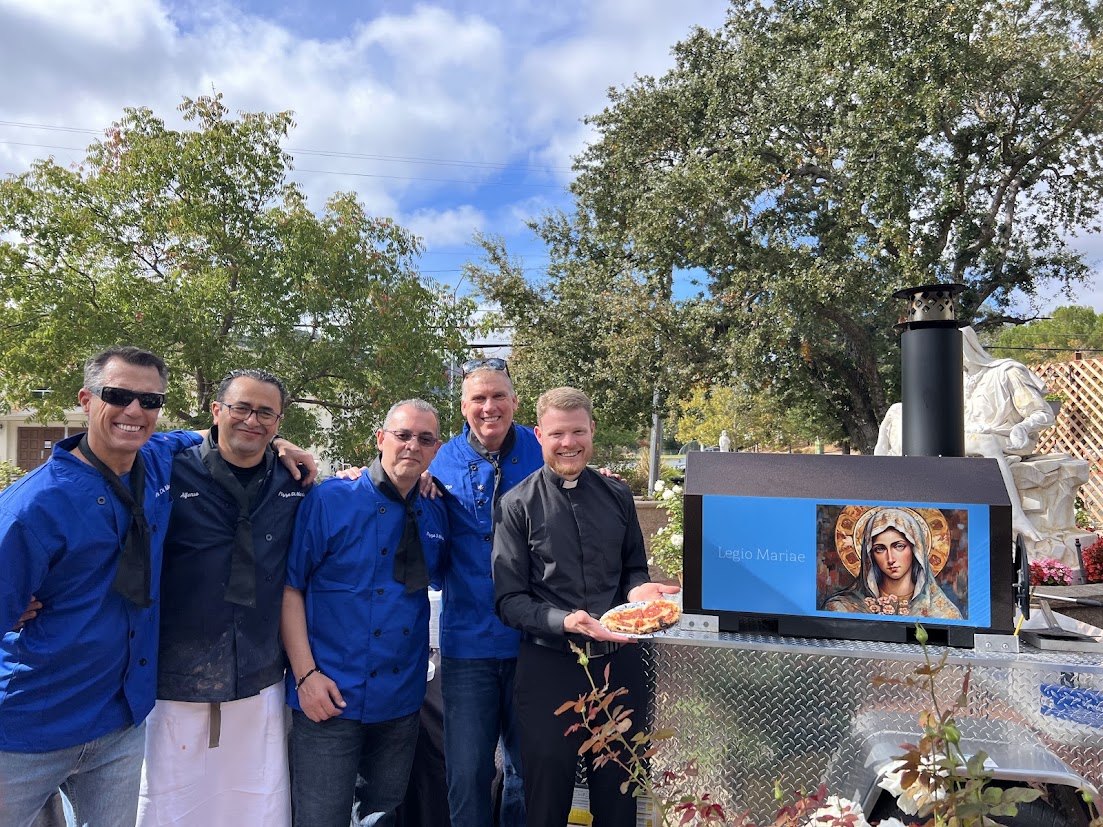 Fr. Matthew with the pizza team in blue chef jackets beside the wood-fired oven